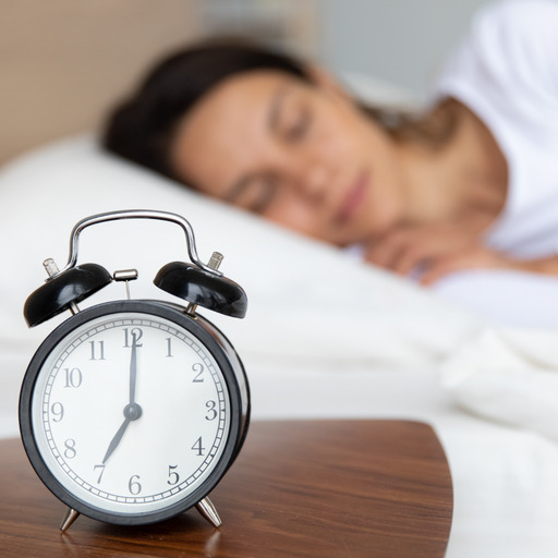Schlafende Frau im Bett, mit einem Wecker auf dem Nachttisch